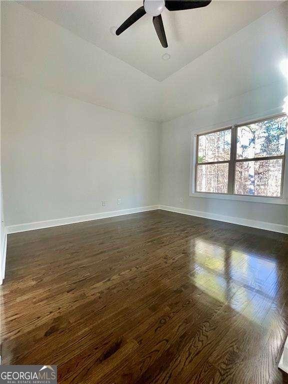 spare room with vaulted ceiling, dark wood-style flooring, a ceiling fan, and baseboards