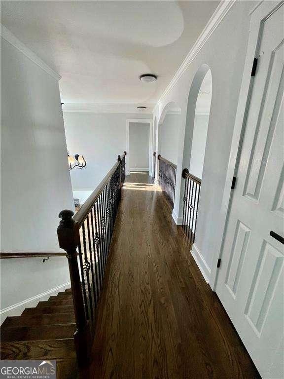 hallway featuring dark wood-style floors, ornamental molding, an upstairs landing, and baseboards