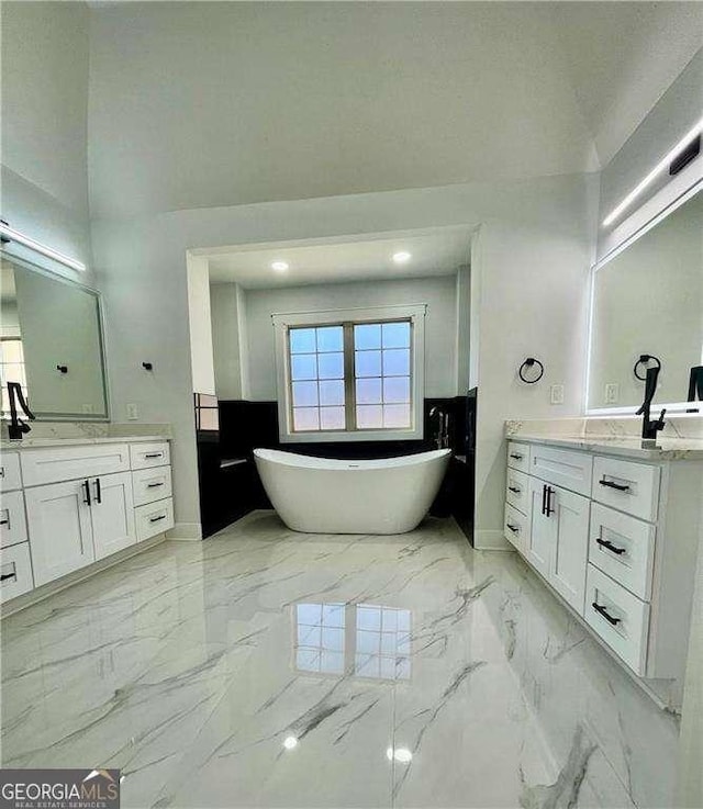 bathroom with a freestanding bath, marble finish floor, two vanities, and a sink