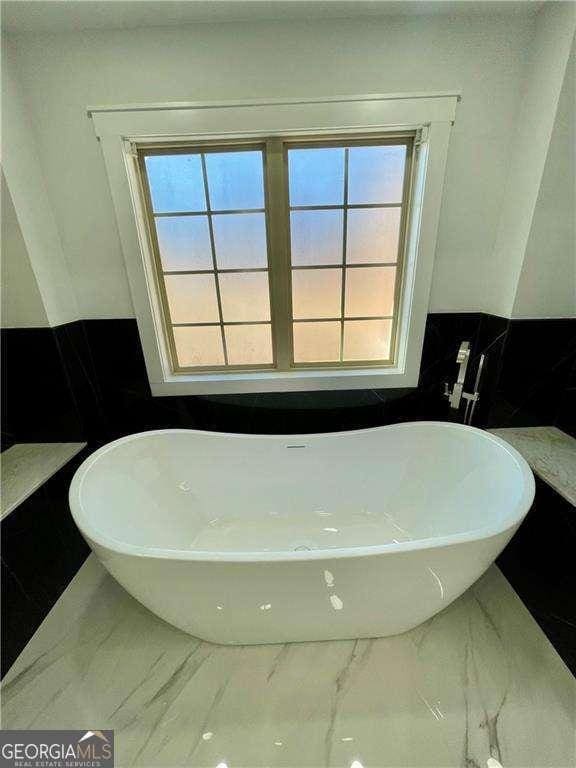 full bathroom with marble finish floor and a soaking tub