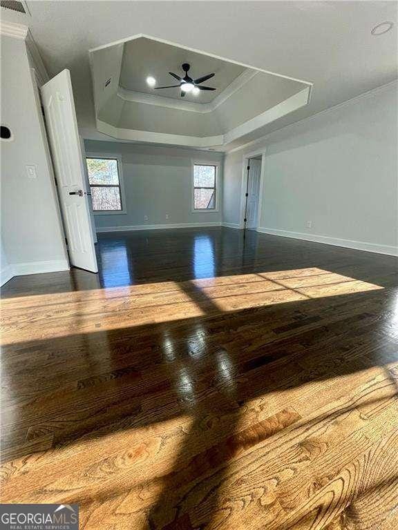 interior space with ceiling fan, baseboards, a raised ceiling, and wood finished floors