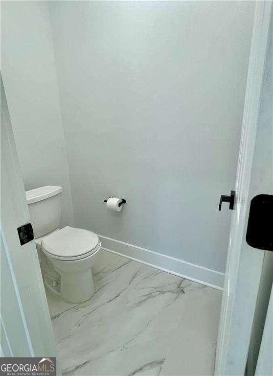 bathroom featuring toilet, marble finish floor, and baseboards