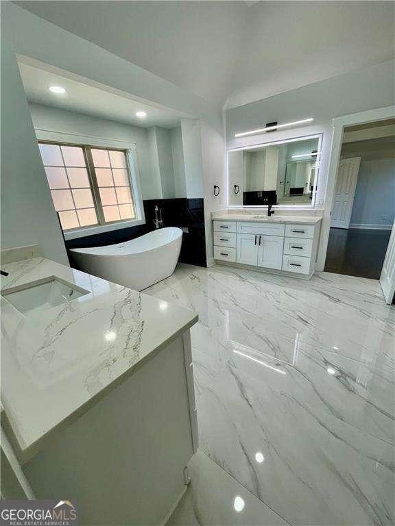 bathroom featuring a soaking tub, marble finish floor, two vanities, and a sink