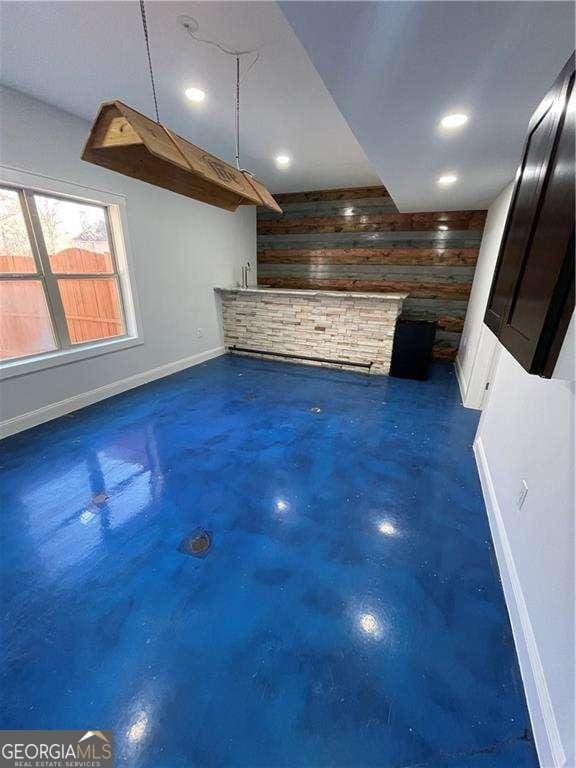 unfurnished living room featuring concrete flooring, wood walls, recessed lighting, and baseboards