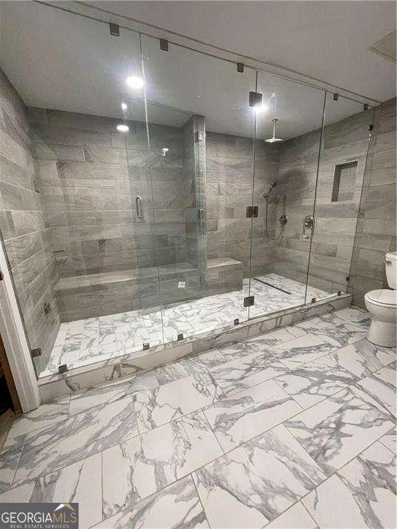 bathroom with marble finish floor, a shower stall, and toilet