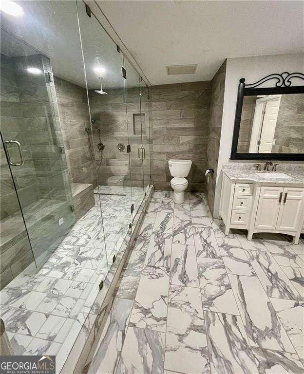 full bath featuring a stall shower, toilet, marble finish floor, a textured ceiling, and vanity