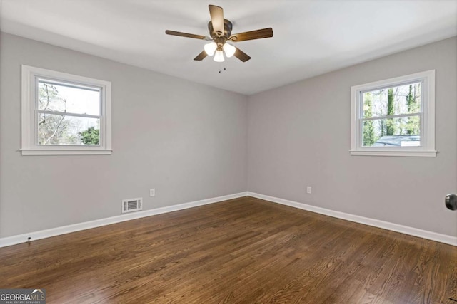 empty room with dark wood-type flooring, visible vents, ceiling fan, and baseboards