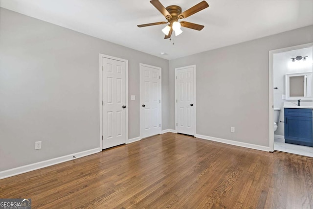 unfurnished bedroom featuring ensuite bathroom, multiple closets, wood finished floors, and baseboards