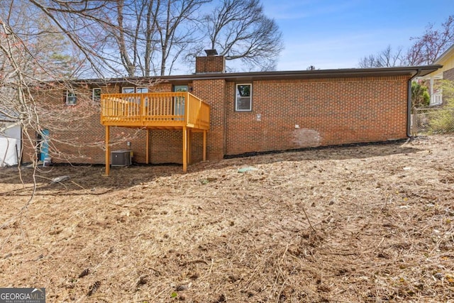 rear view of house featuring a chimney, central AC unit, a deck, and brick siding