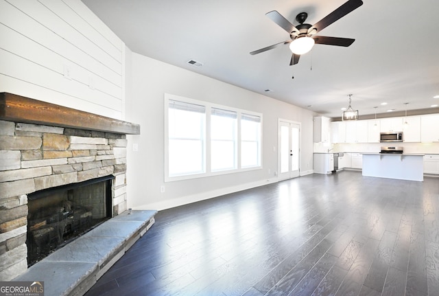 unfurnished living room featuring visible vents, a stone fireplace, dark wood-style floors, and a ceiling fan