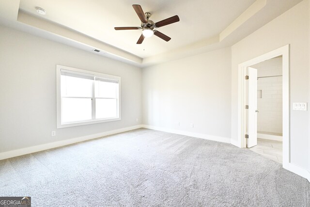 empty room with a ceiling fan, carpet, baseboards, visible vents, and a tray ceiling