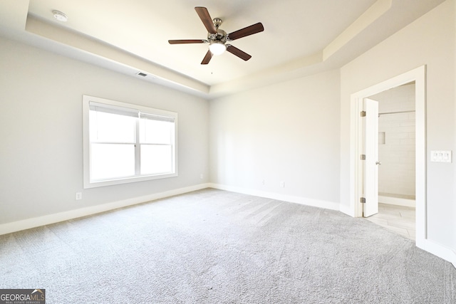 carpeted empty room featuring a raised ceiling, ceiling fan, and baseboards