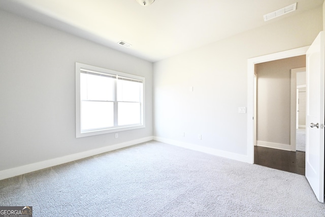 spare room featuring visible vents, baseboards, and dark colored carpet