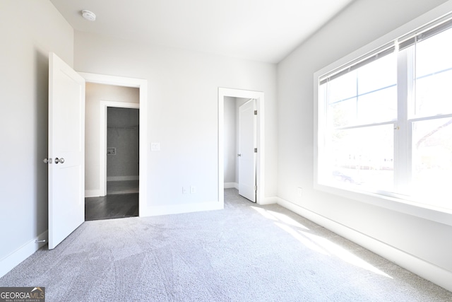 unfurnished bedroom with a walk in closet, multiple windows, carpet flooring, and baseboards