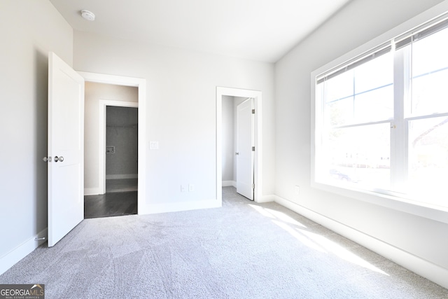 unfurnished bedroom with carpet floors, a walk in closet, and baseboards