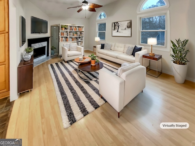 living area with lofted ceiling, a fireplace, a ceiling fan, baseboards, and light wood-style floors