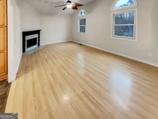 unfurnished living room with baseboards, ceiling fan, wood finished floors, vaulted ceiling, and a high end fireplace