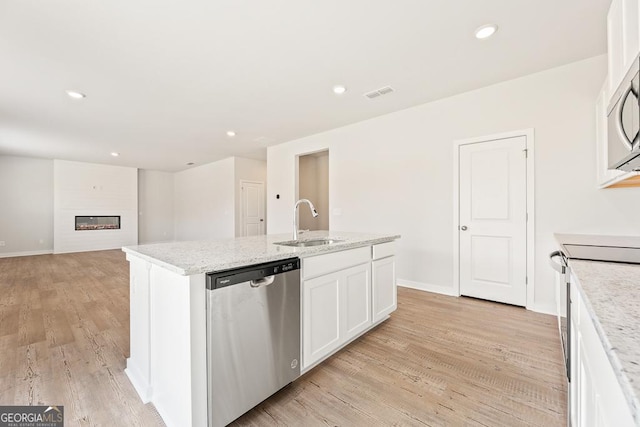 kitchen featuring a kitchen island with sink, stainless steel appliances, a sink, visible vents, and a glass covered fireplace