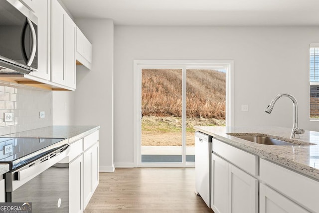 kitchen with tasteful backsplash, light wood-style flooring, light stone counters, stainless steel appliances, and a sink