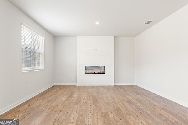 unfurnished living room featuring baseboards, a fireplace, visible vents, and light wood finished floors