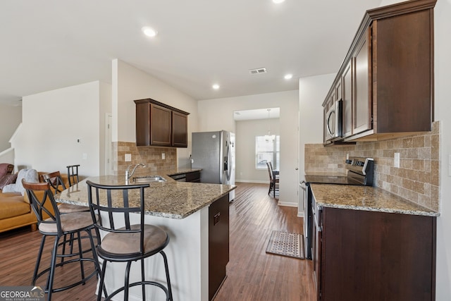 kitchen with dark wood finished floors, dark brown cabinetry, a kitchen breakfast bar, stainless steel appliances, and a sink