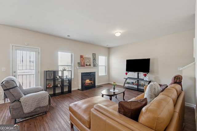 living area with a glass covered fireplace, visible vents, and dark wood-style flooring