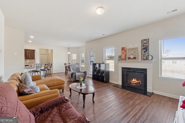 living area featuring wood finished floors, visible vents, baseboards, recessed lighting, and a glass covered fireplace