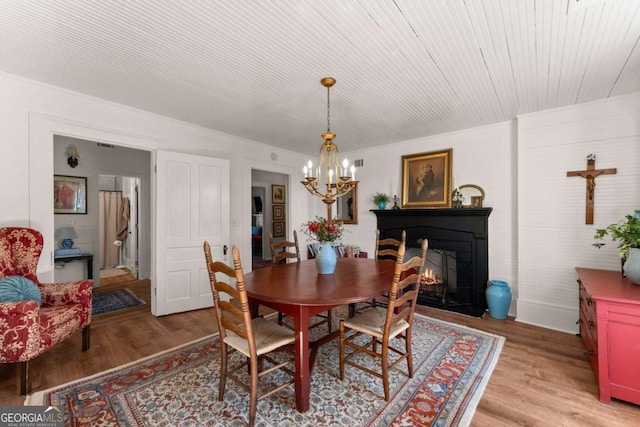 dining space featuring an inviting chandelier, a fireplace with flush hearth, and light wood-style floors