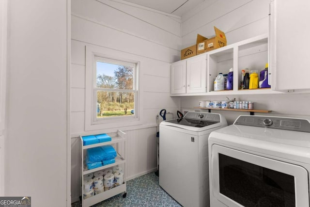 clothes washing area featuring wood walls, washing machine and clothes dryer, and cabinet space