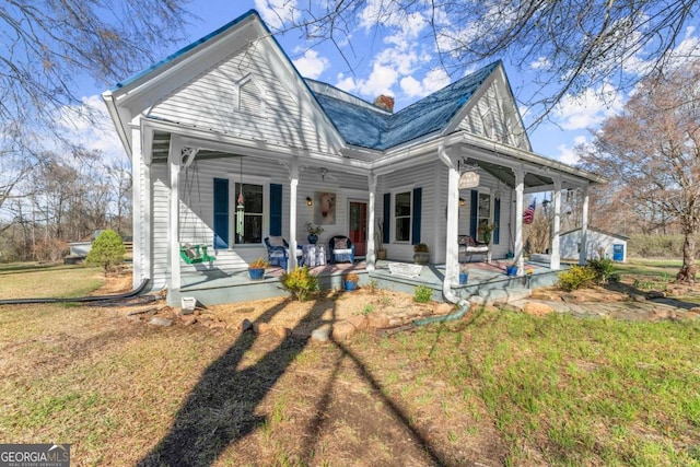 rear view of property featuring covered porch, a chimney, and a lawn