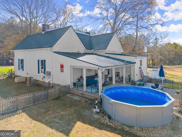 back of property featuring metal roof, a fenced backyard, an outdoor living space, a fenced in pool, and a chimney