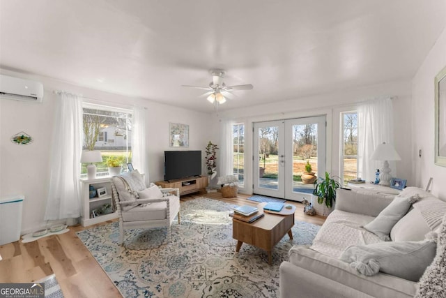 living area with french doors, a wealth of natural light, a wall mounted air conditioner, and light wood-style flooring