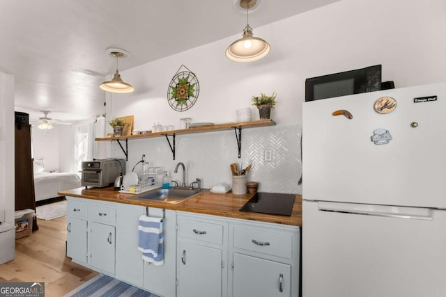 kitchen with open shelves, butcher block counters, backsplash, freestanding refrigerator, and a sink