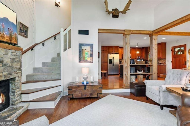 living room with a high ceiling, a fireplace, wood finished floors, visible vents, and ornate columns