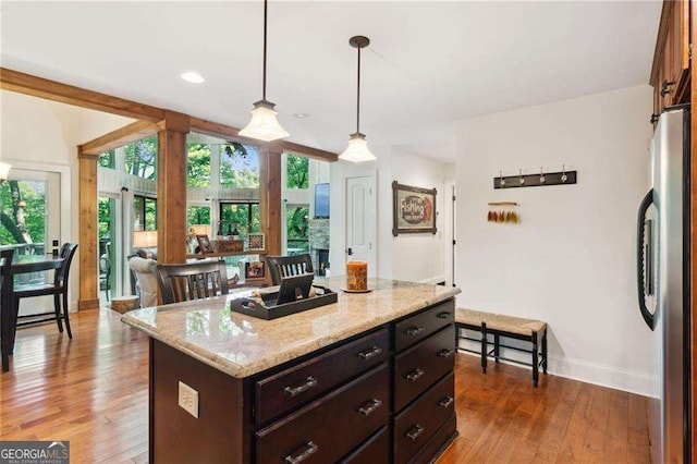 kitchen with baseboards, wood finished floors, freestanding refrigerator, light stone countertops, and pendant lighting