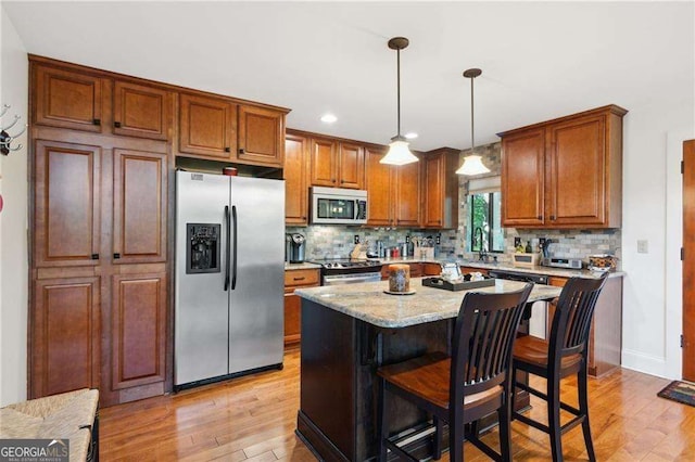 kitchen with a kitchen breakfast bar, appliances with stainless steel finishes, light wood finished floors, decorative light fixtures, and tasteful backsplash