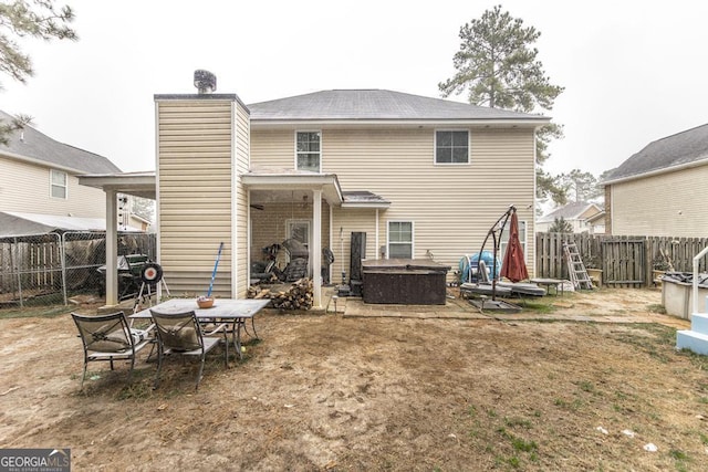 back of house with a chimney, a patio area, a fenced backyard, and a hot tub