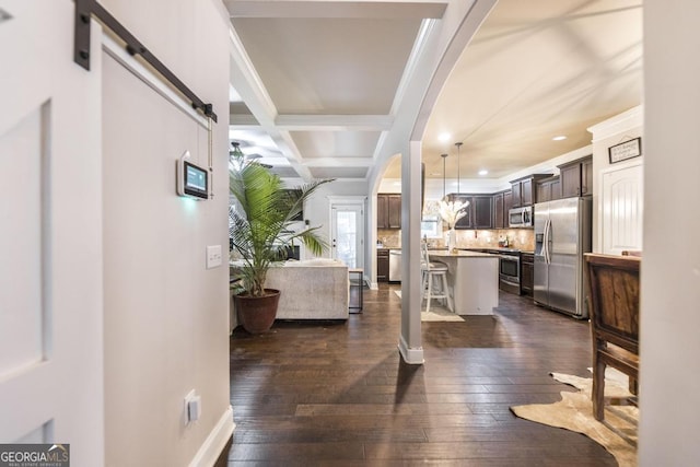 interior space with arched walkways, a barn door, dark wood-style flooring, coffered ceiling, and beamed ceiling