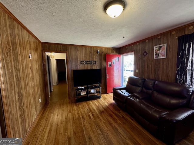 living area with wood walls, crown molding, a textured ceiling, and wood finished floors