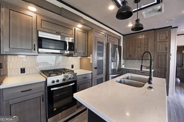 kitchen featuring stainless steel appliances, tasteful backsplash, light countertops, a sink, and wood finished floors