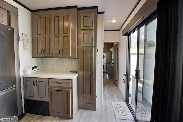 kitchen with light countertops, ornamental molding, light wood-type flooring, and freestanding refrigerator