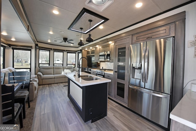 kitchen with a center island with sink, stainless steel appliances, light countertops, open floor plan, and a sink