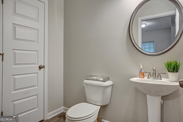 half bathroom featuring wood finished floors, toilet, and baseboards