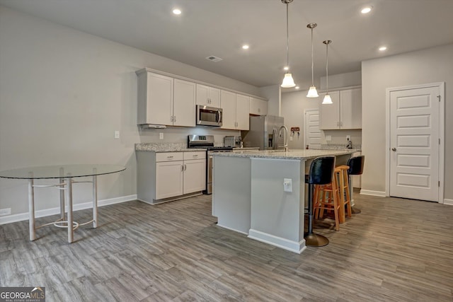 kitchen with white cabinets, a center island with sink, stainless steel appliances, and wood finished floors