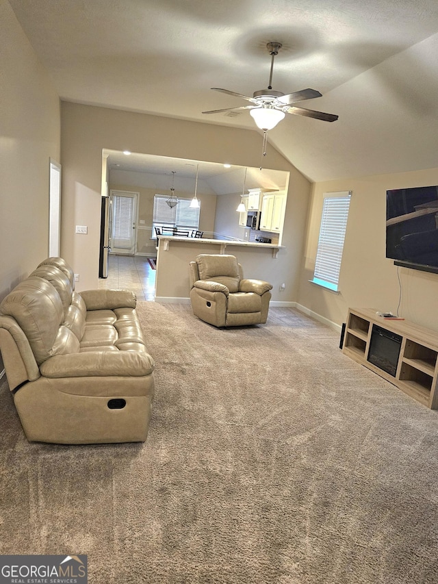 living room featuring light carpet, baseboards, a ceiling fan, vaulted ceiling, and a wealth of natural light