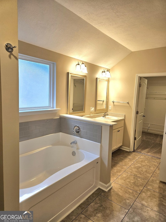 bathroom featuring a textured ceiling, vanity, vaulted ceiling, a bath, and tile patterned floors