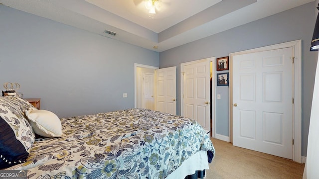 bedroom featuring visible vents, a tray ceiling, and light colored carpet