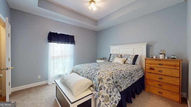 bedroom featuring a tray ceiling, light colored carpet, and baseboards