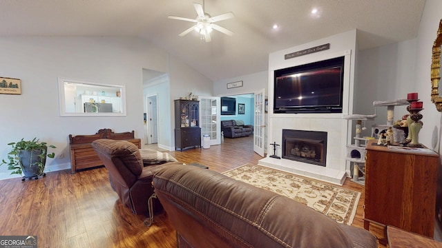 living area with a fireplace with raised hearth, vaulted ceiling, wood finished floors, and a ceiling fan