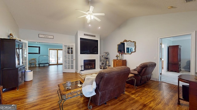 living area featuring lofted ceiling, a ceiling fan, a fireplace with raised hearth, and wood finished floors